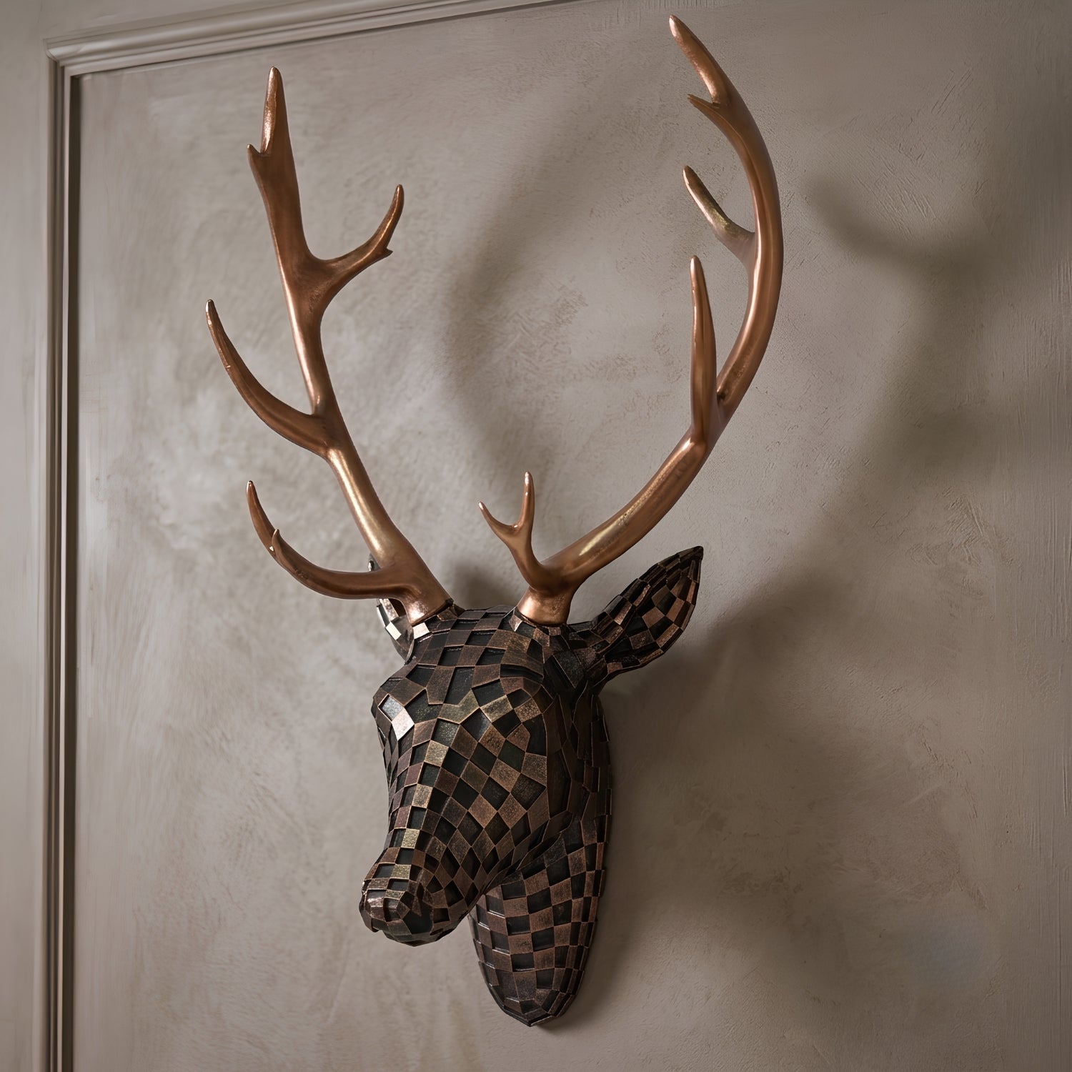 A decorative stag head wall mount with large antlers, featuring a geometric mosaic pattern on the head and a metallic copper finish on the antlers, mounted on a textured beige wall.