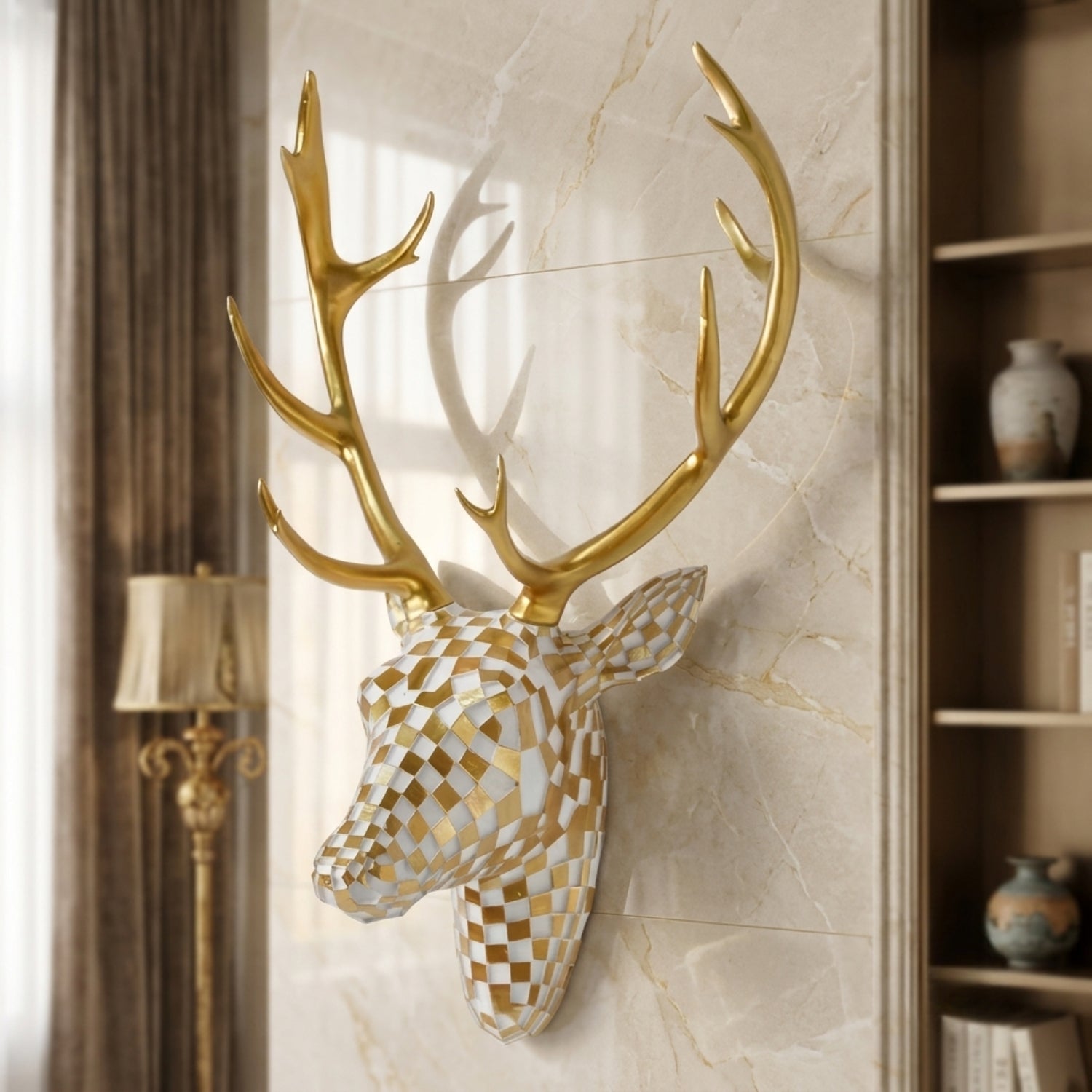 A decorative stag head wall mount with large gold antlers and a geometric checkered head in white and gold, displayed on a beige marble wall in an interior room setting.