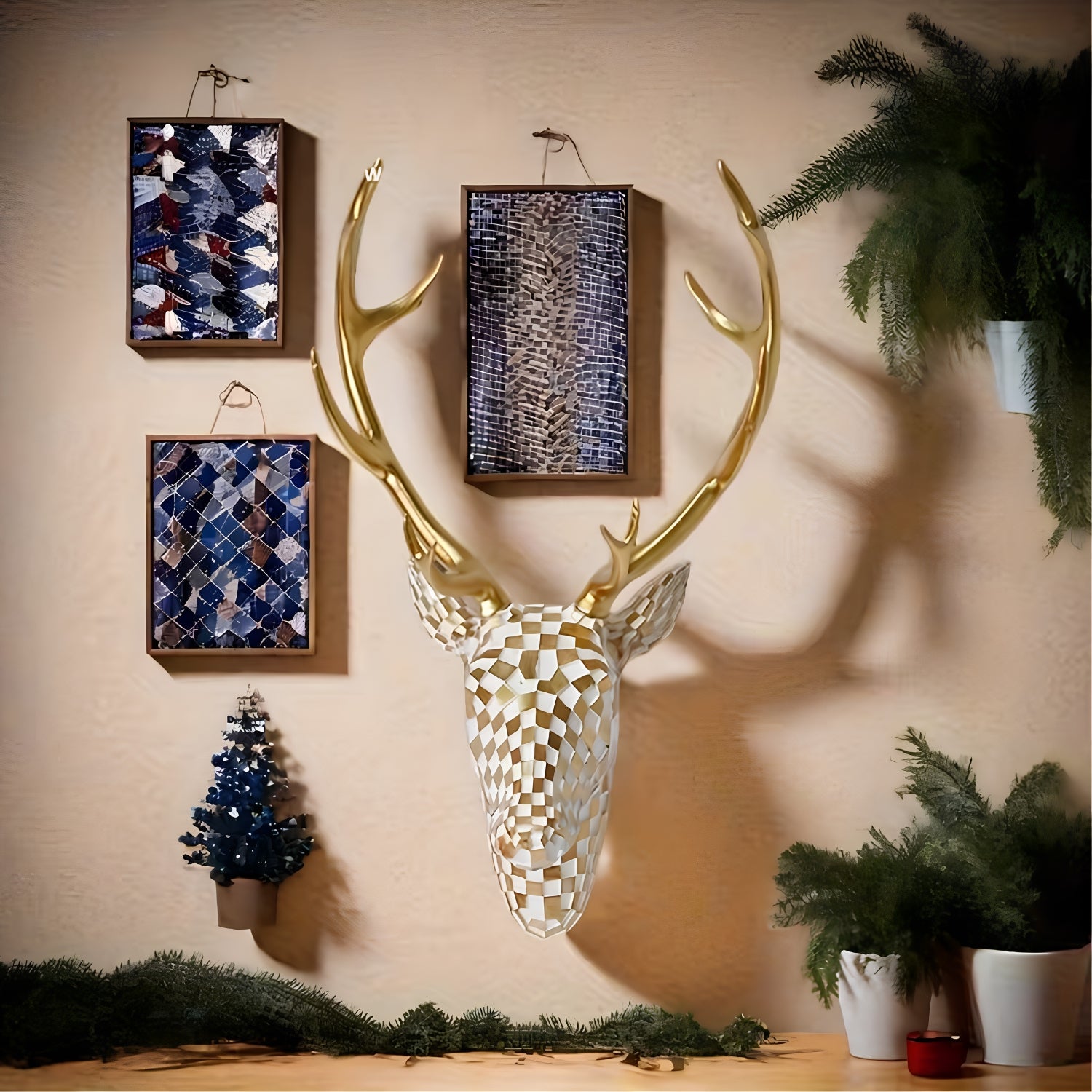 A decorative stag head wall mount with large gold antlers, featuring a geometric patterned face in white and gold. The stag is displayed on a beige wall alongside three framed abstract art pieces, a small blue Christmas tree, and potted green plants.