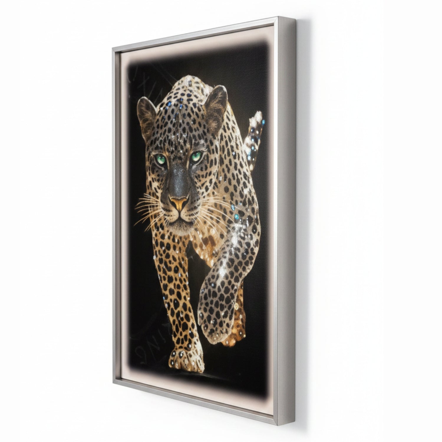 A framed wall art print featuring a detailed leopard with green eyes on a black background, shown hanging on a white wall.