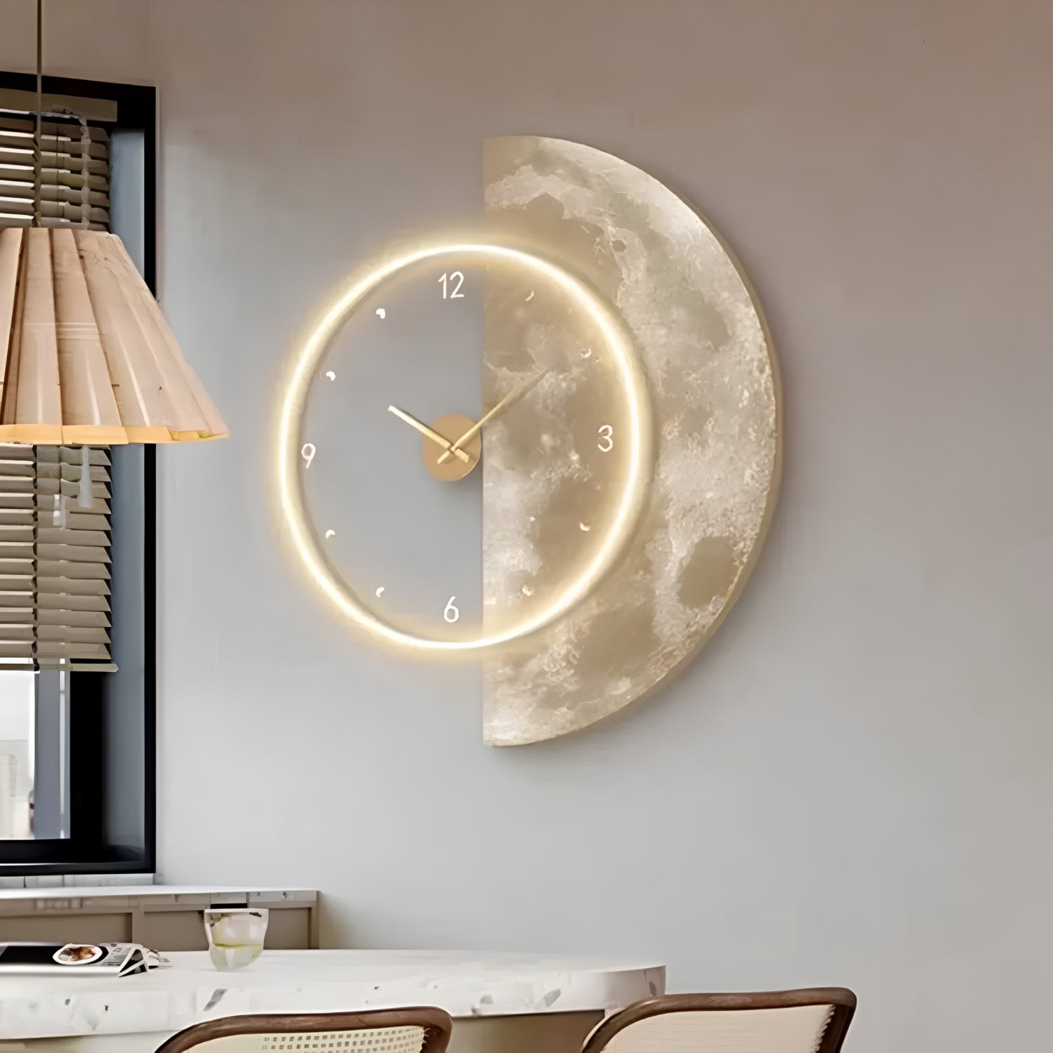 A modern half-moon wall clock with a textured gold and silver finish, featuring a glowing LED ring and gold hands, mounted on a light gray wall in a dining room setting.