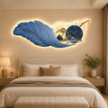 A large decorative wall art piece mounted above a bed in a bedroom. The artwork shows a glowing blue feather with a built-in clock, small trees, birds, and warm light around it.