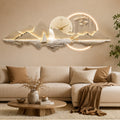 A decorative wall clock featuring a glowing illuminated mountain and water scene with a central round clock face, mounted above a beige sofa in a styled living room.