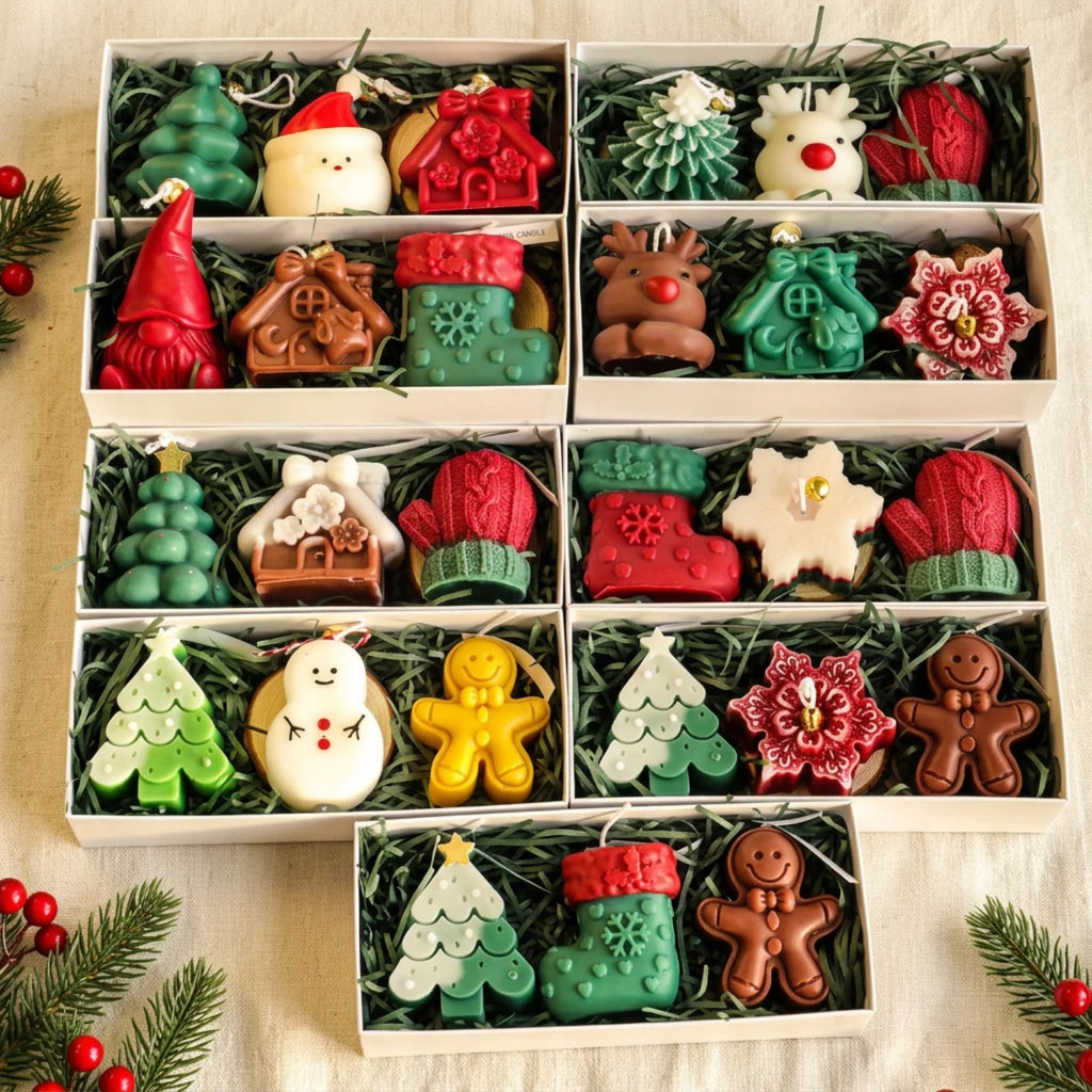 Six white gift boxes filled with Christmas-themed wax melts or soaps arranged in a grid, featuring shapes like trees, snowman, gingerbread, Santa, reindeer, mittens, boots, and floral ornaments, set on a beige fabric with pine branches and red berries.