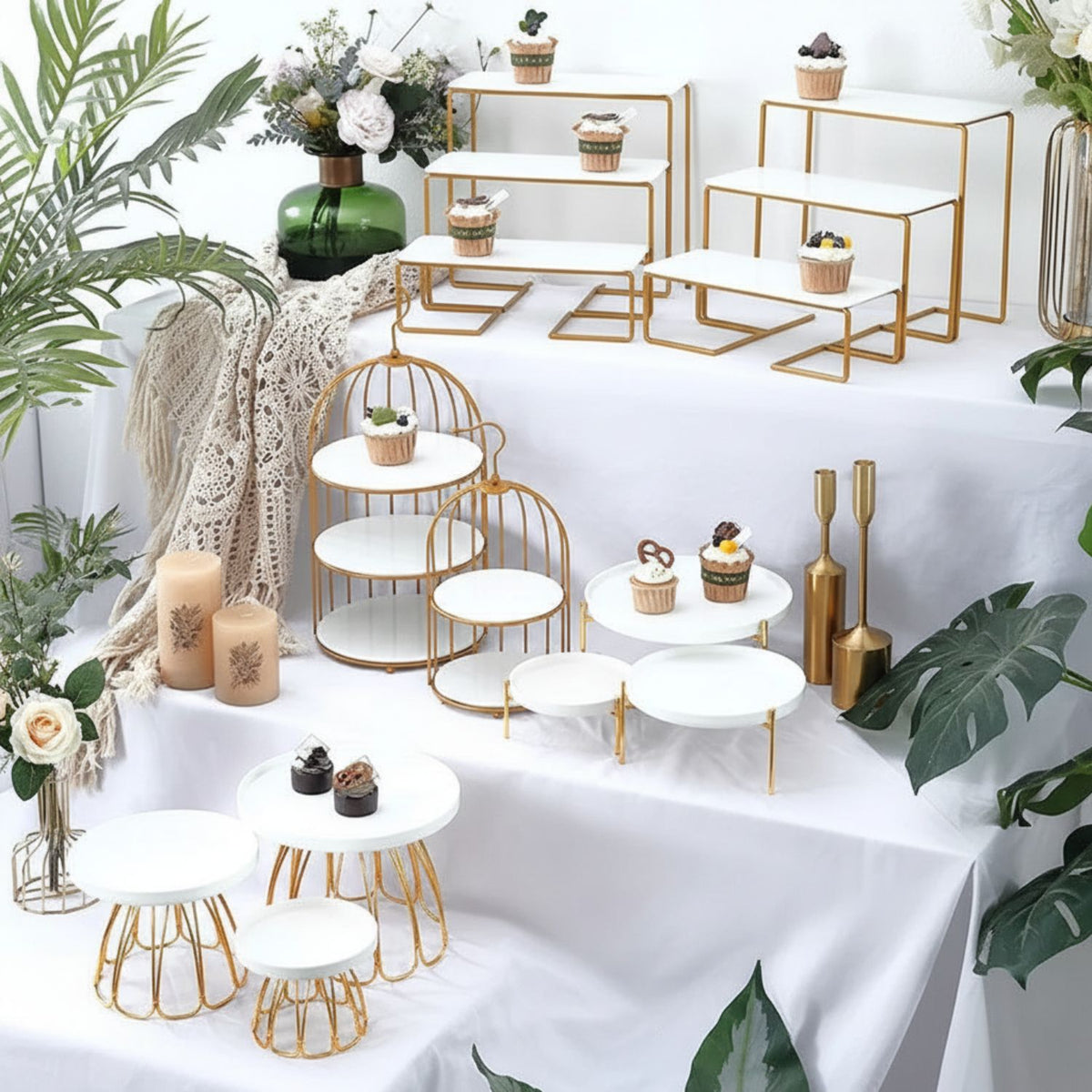 Decorative setup with gold and white tables, plants, and candles on a white background