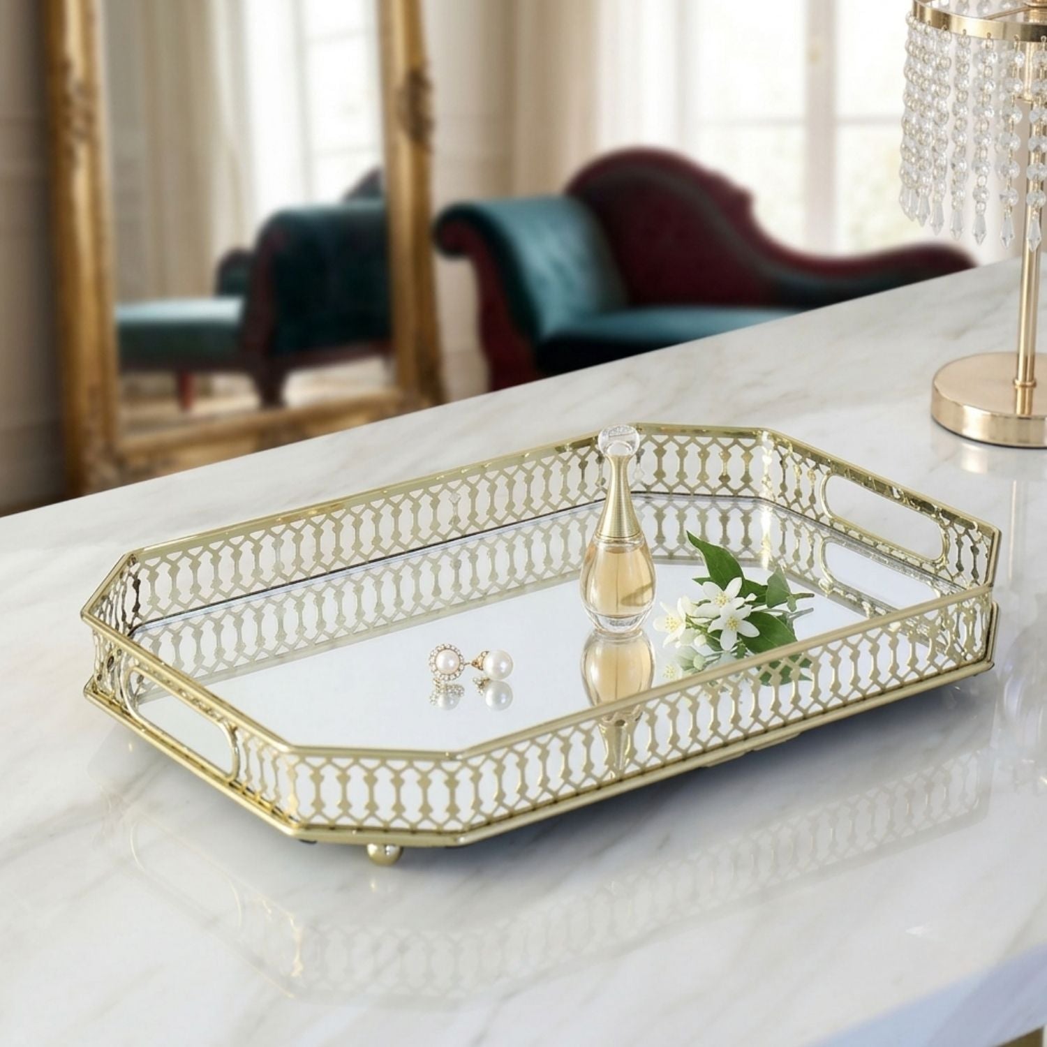 A rectangular mirrored tray with a gold metal frame and decorative cutout edges, styled on a white marble table in a bright interior setting.