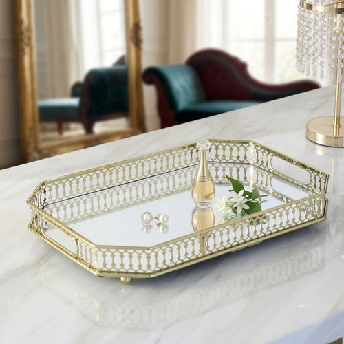 A rectangular mirrored tray with a gold metal frame and decorative cutout edges, styled on a white marble table in a bright interior setting.