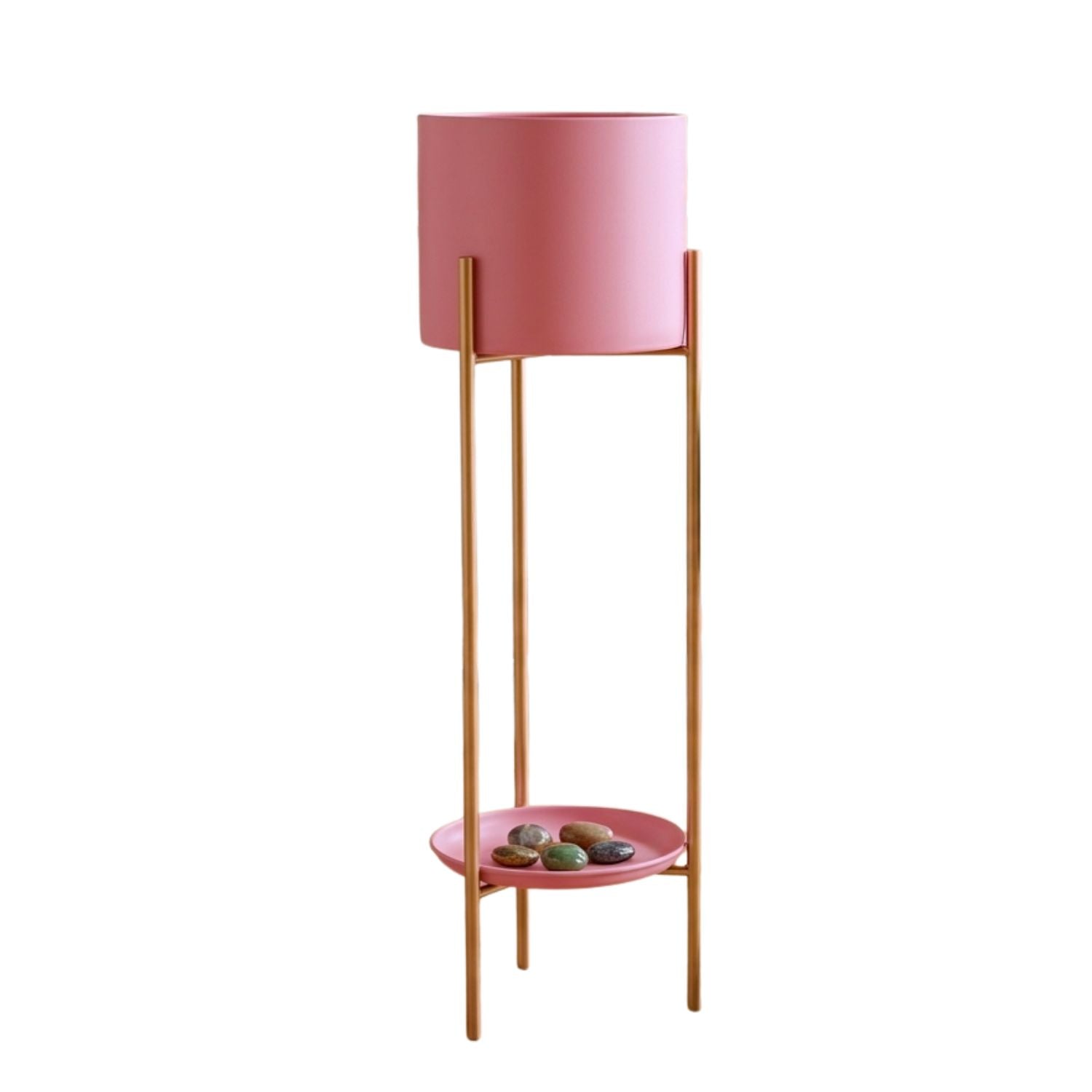 A modern two-tier plant stand featuring a cylindrical pink top pot holder and a shallow oval pink bottom tray with decorative stones, supported by slim gold metal legs against a plain white background.