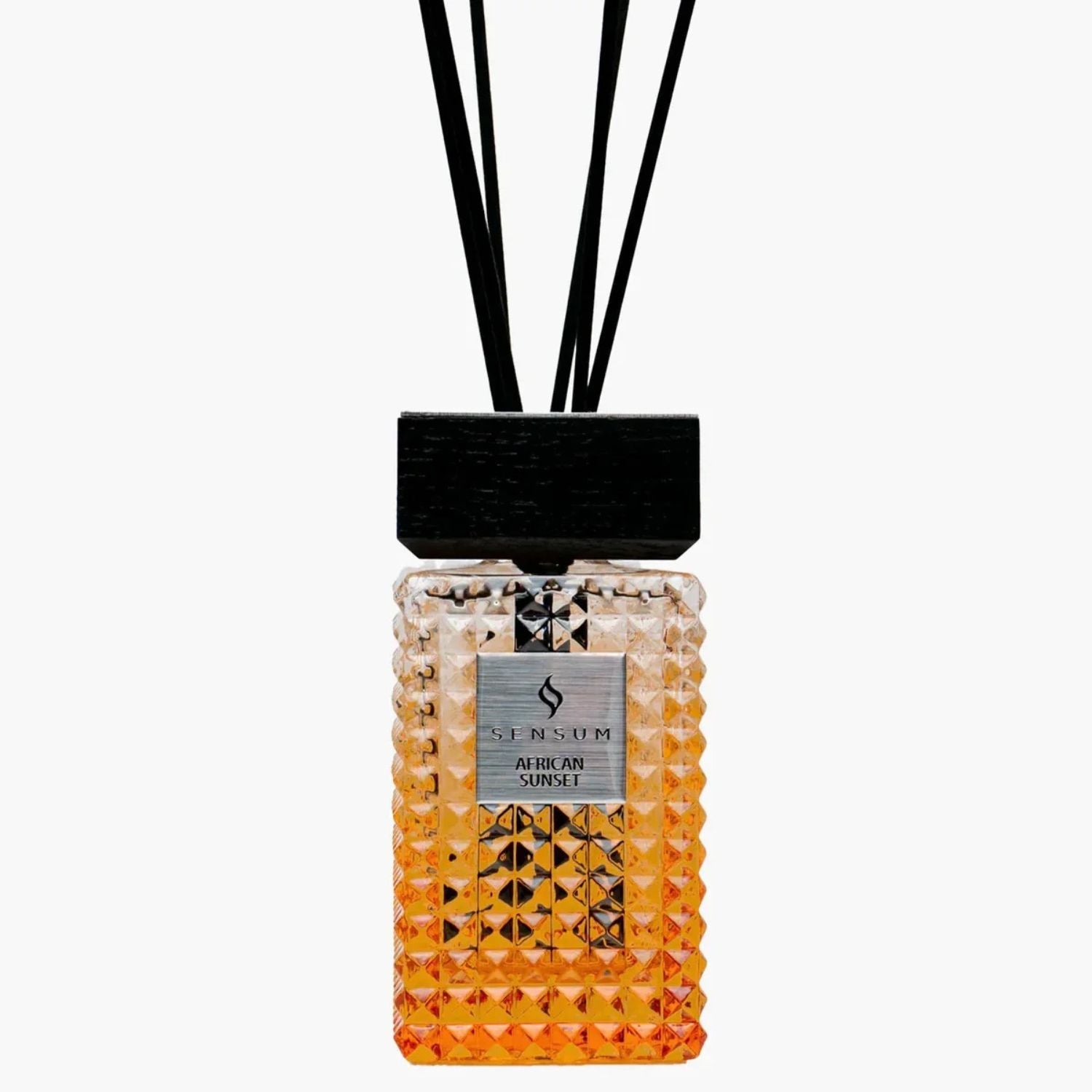 A reed diffuser bottle with a faceted textured glass body that transitions from clear at the top to orange at the bottom, featuring a black cap and black reeds, on a light gray background.