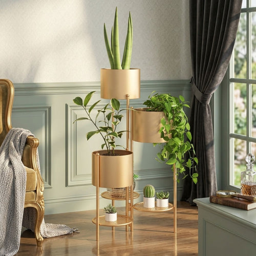 A three-tier gold metal plant stand styled in a bright room with green plants, a gold armchair, and a window with dark curtains.