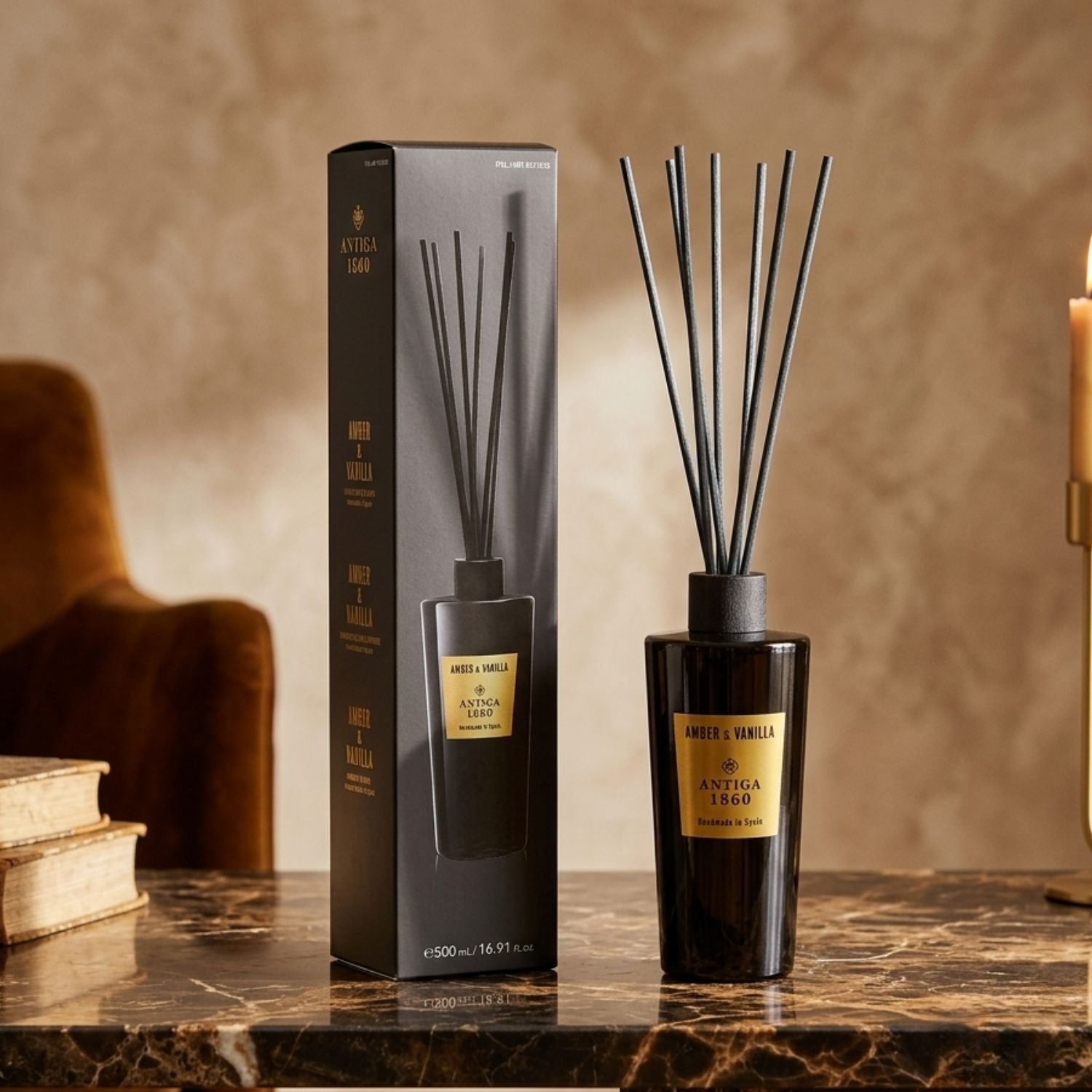 A reed diffuser bottle with black reeds stands beside its matching black box on a polished marble surface. The bottle and box are dark glass with a gold label reading 'Amber & Vanilla SYNTIGA 1950'.