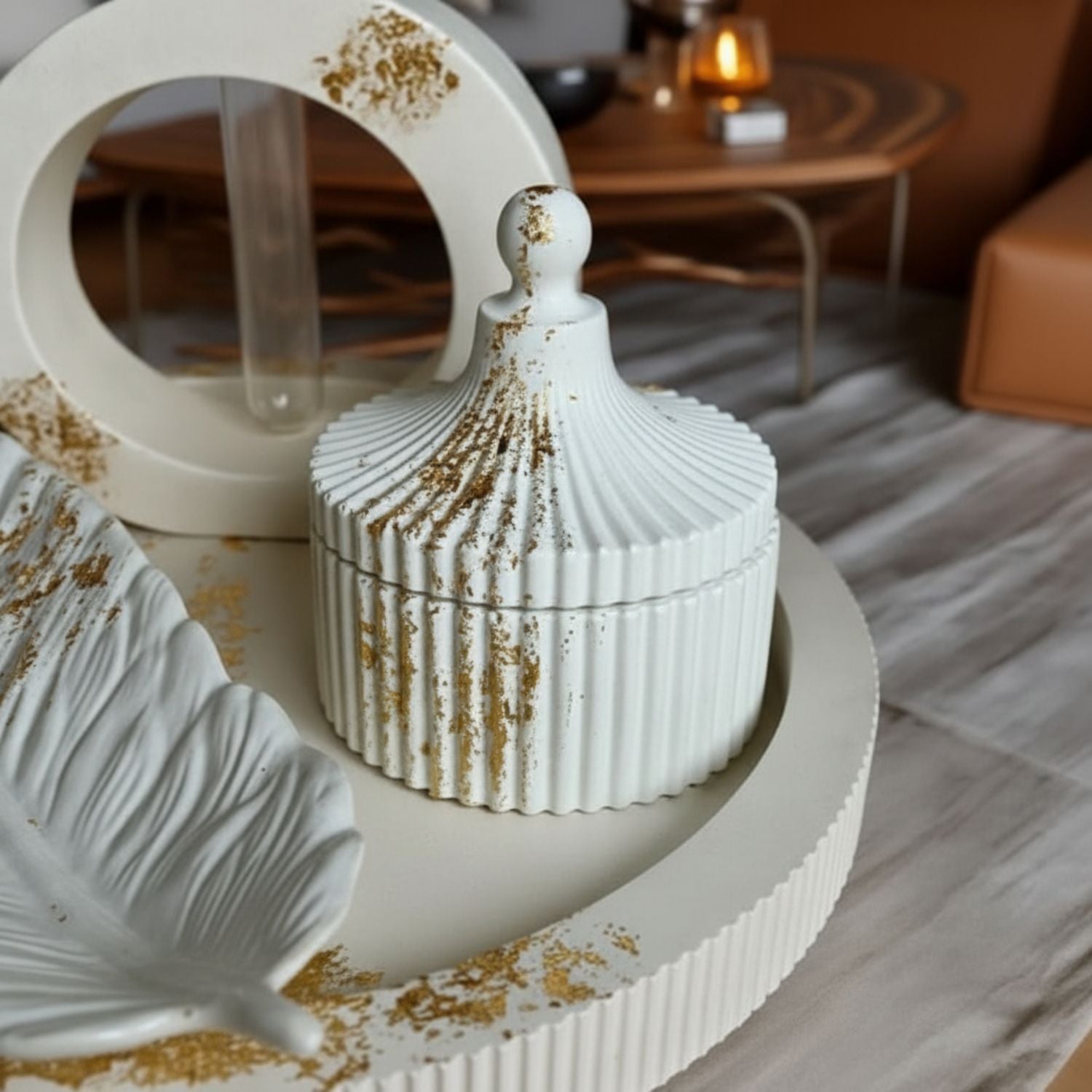A white ribbed ceramic lidded jar with a small knob top, decorated with scattered gold leaf flakes, displayed on a matching round tray in a styled interior setting.