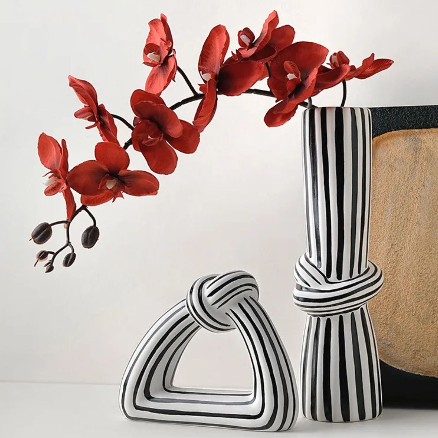 Three black and white striped ceramic decorative vases arranged on a white surface against a light gray background, with a red artificial orchid branch placed in the tall vase.