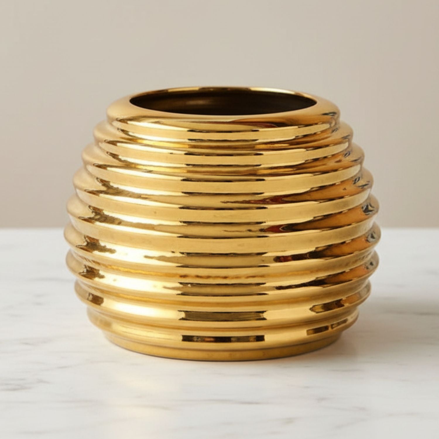 A shiny gold ribbed ceramic vase with a flared rim, displayed on a white marble surface against a neutral beige background.