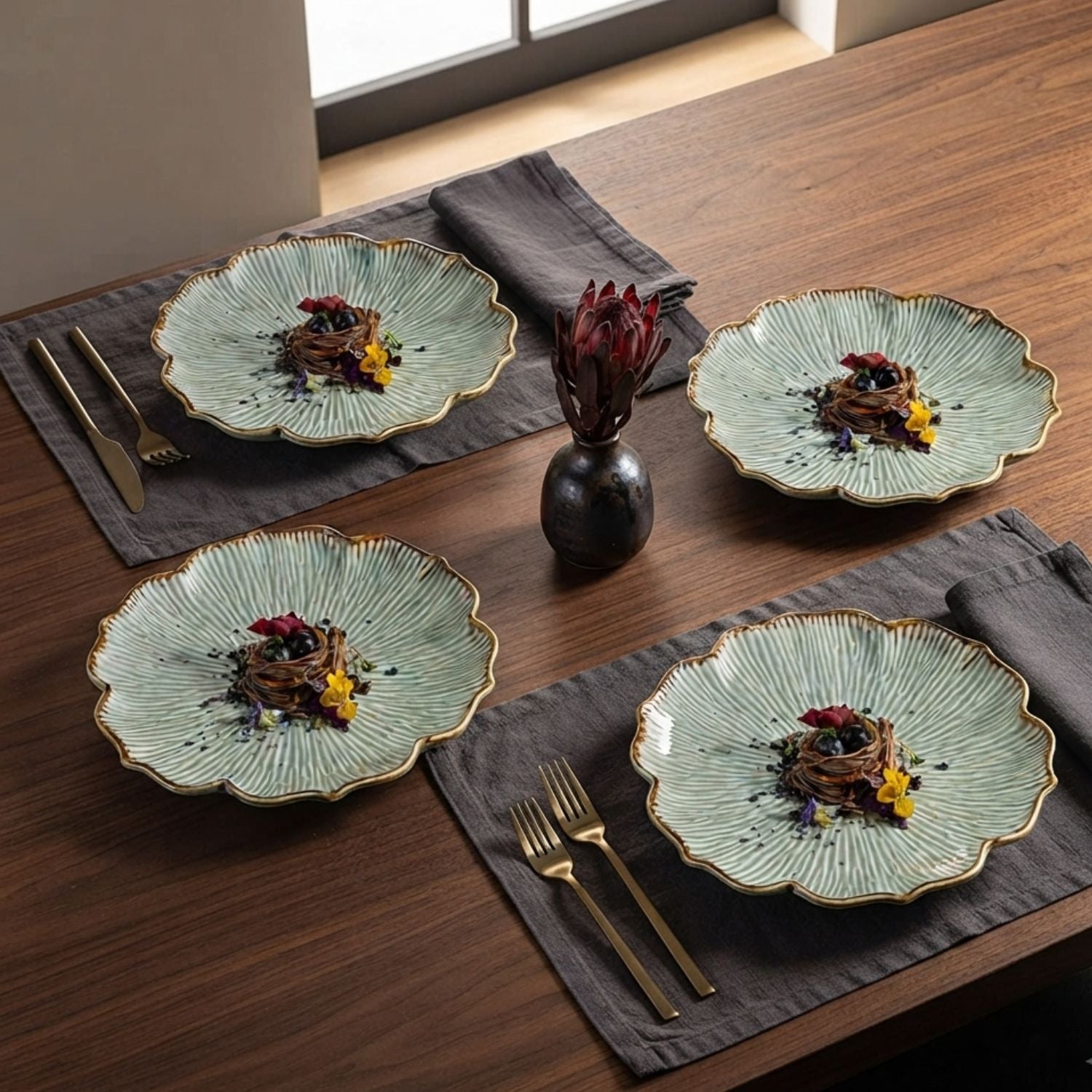 Four scalloped ceramic plates with a light green textured glaze and gold trim, arranged on a dark wood table with gray placemats and gold-toned cutlery.