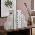 White cloud-shaped bookends holding three books on a wooden console table in a styled room with a pink wall, framed art, a vase, and a chair.