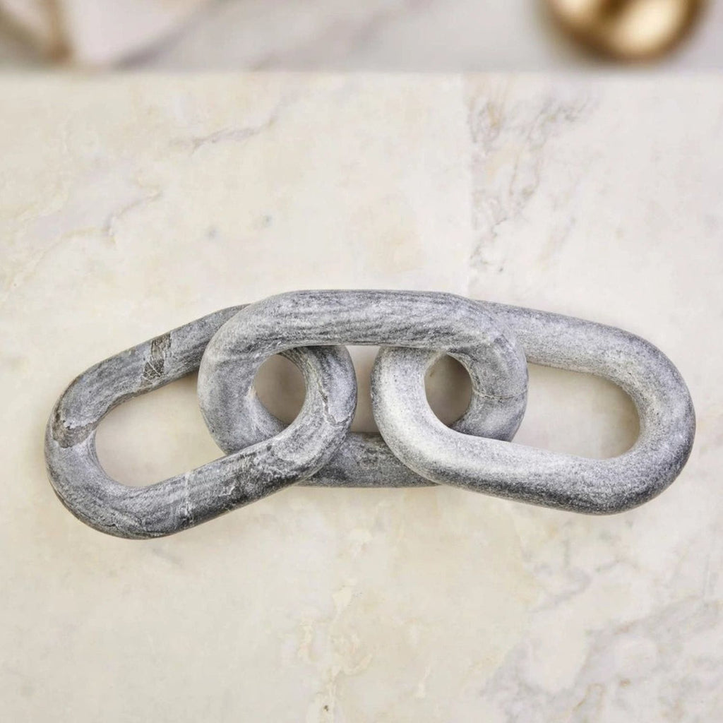 A rustic, distressed gray metal link decor piece resting on a light beige marble surface.