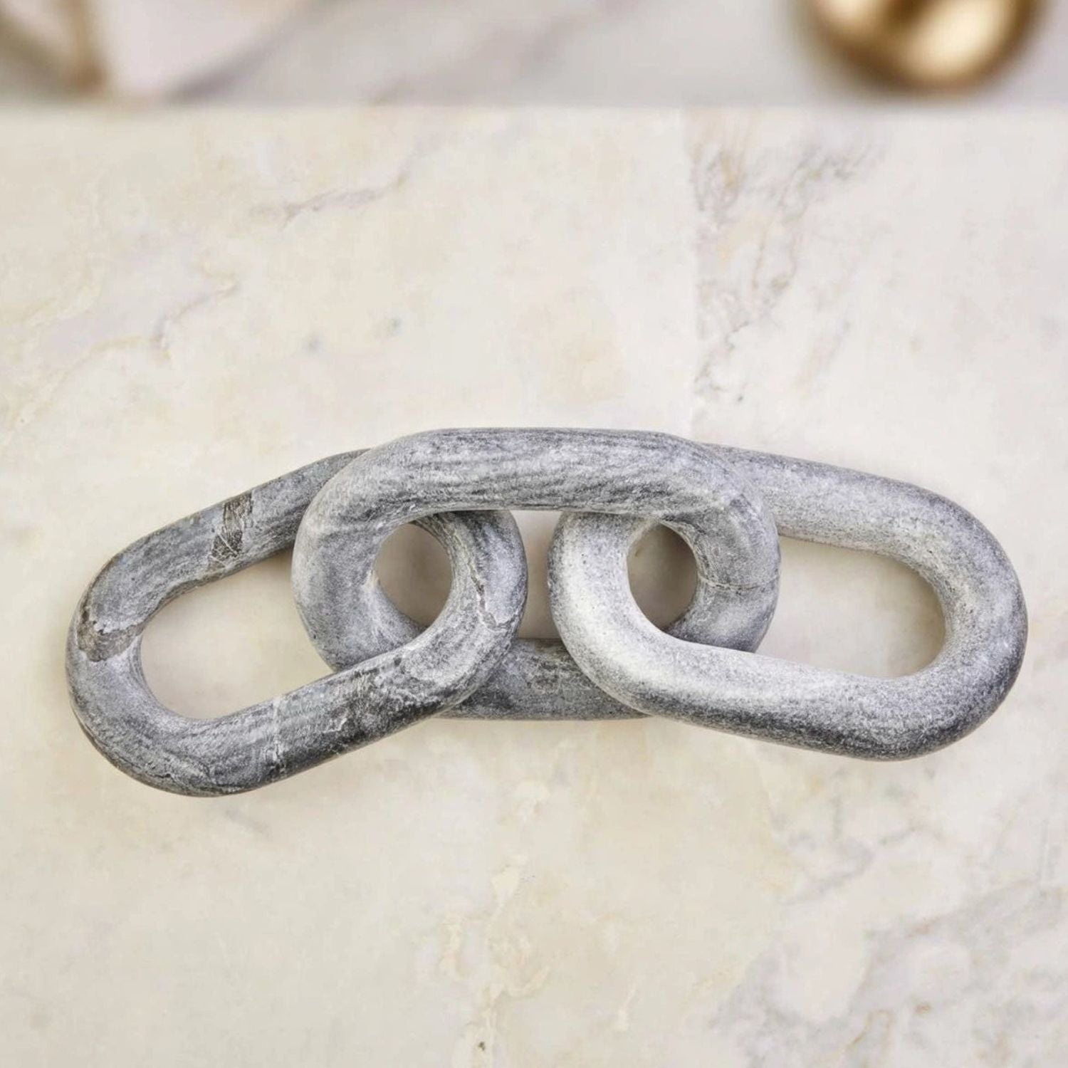 A rustic, distressed gray metal link decor piece resting on a light beige marble surface.