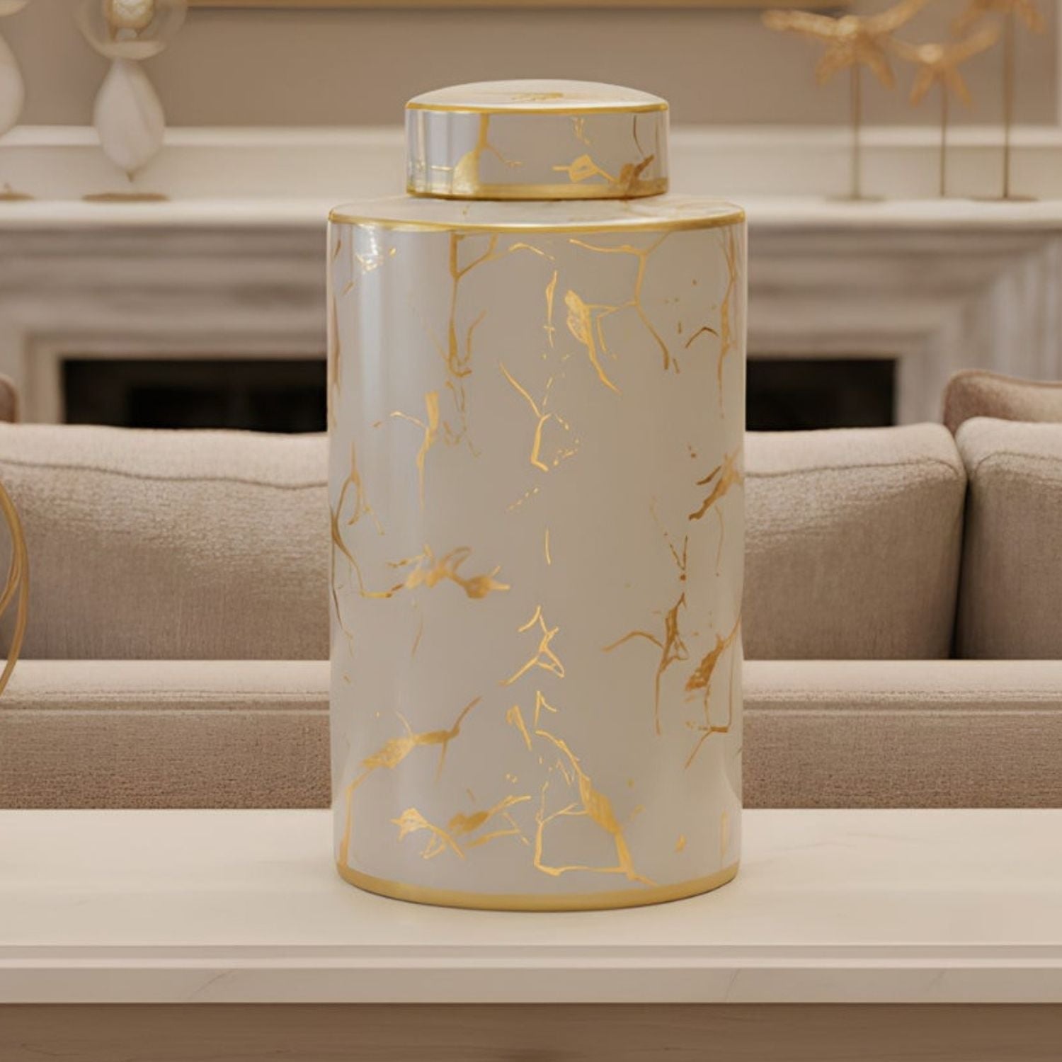A cylindrical ceramic jar with a matching lid, featuring a white marble pattern with metallic gold veins, displayed on a light-colored table in a modern living room setting.