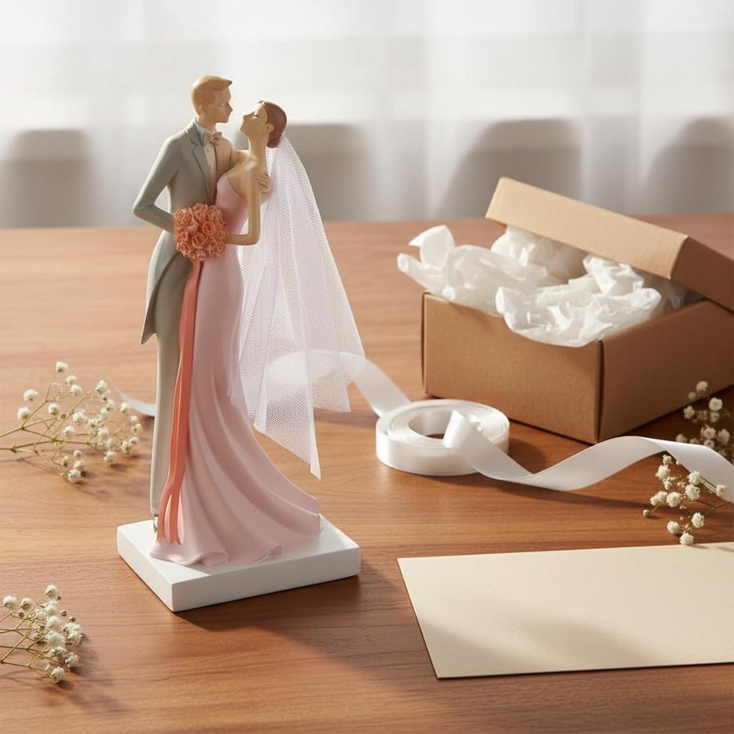 Pink wedding couple figurine styled on wooden table with gift box, ribbon and gypsophila flowers