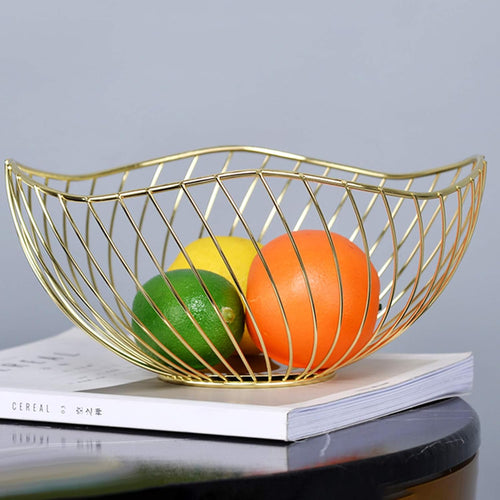 Gold wire metal fruit basket on white surface with fruit