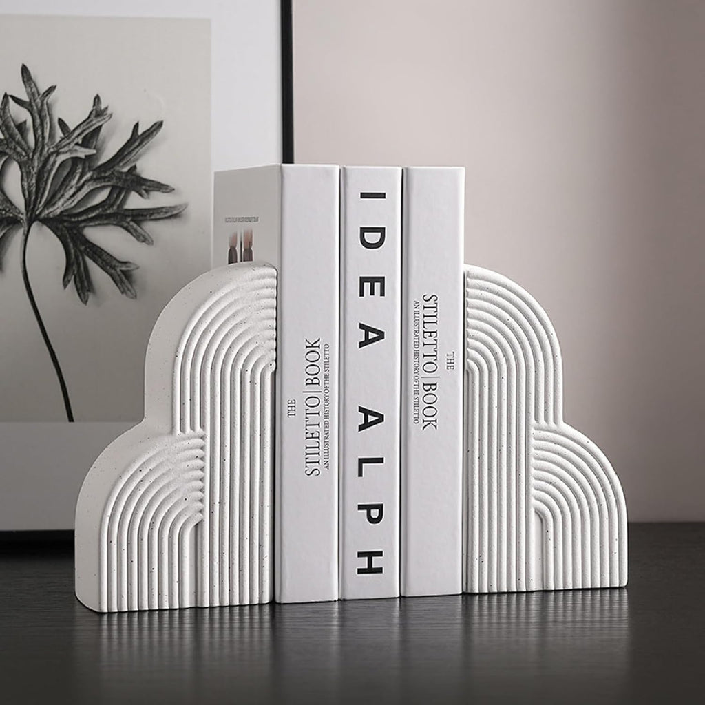 White arch ceramic bookends holding books on dark shelf with botanical art print background
