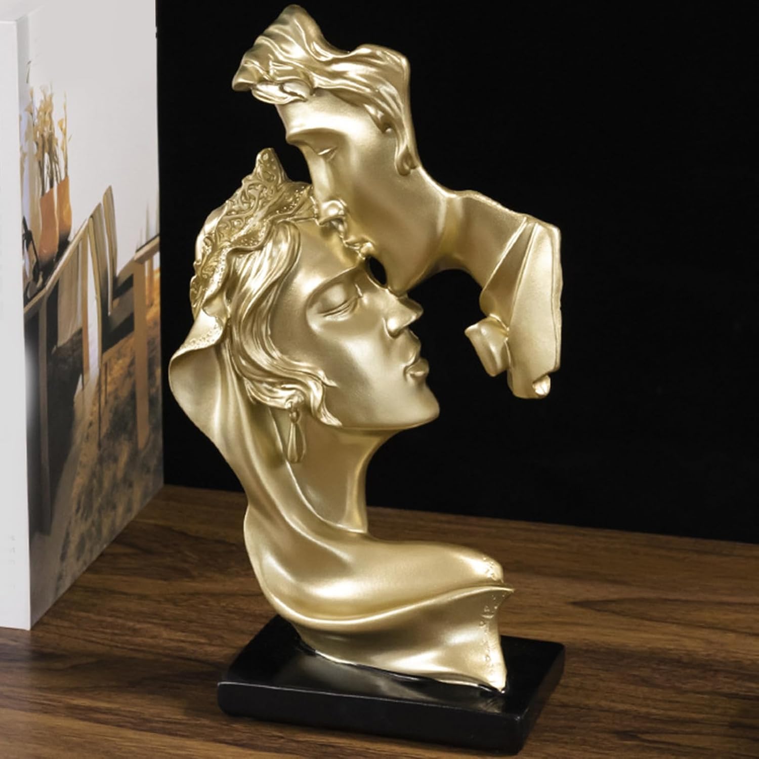 Gold kissing couple forehead sculpture - side view showing flowing hair and draped fabric detail on dark background
