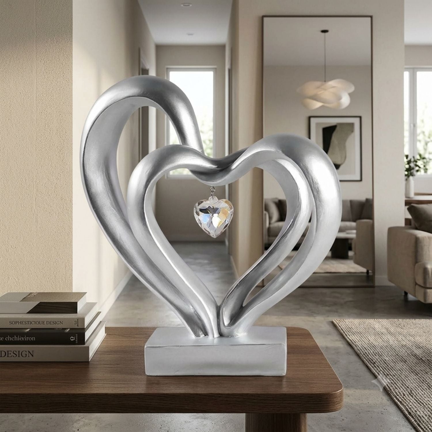 A modern silver heart-shaped metal sculpture with a clear faceted crystal hanging in the center, displayed on a wooden table in a stylishly decorated living room.