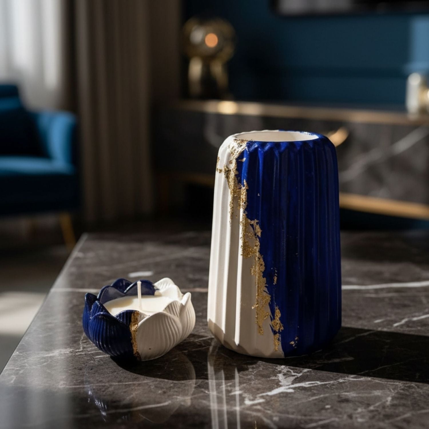 A decorative ceramic vase with a deep cobalt blue and white color scheme, featuring a gold leaf crackle design along the seam. The vase is shown standing on a dark marble table next to its matching lid, with a blurred modern living room background.