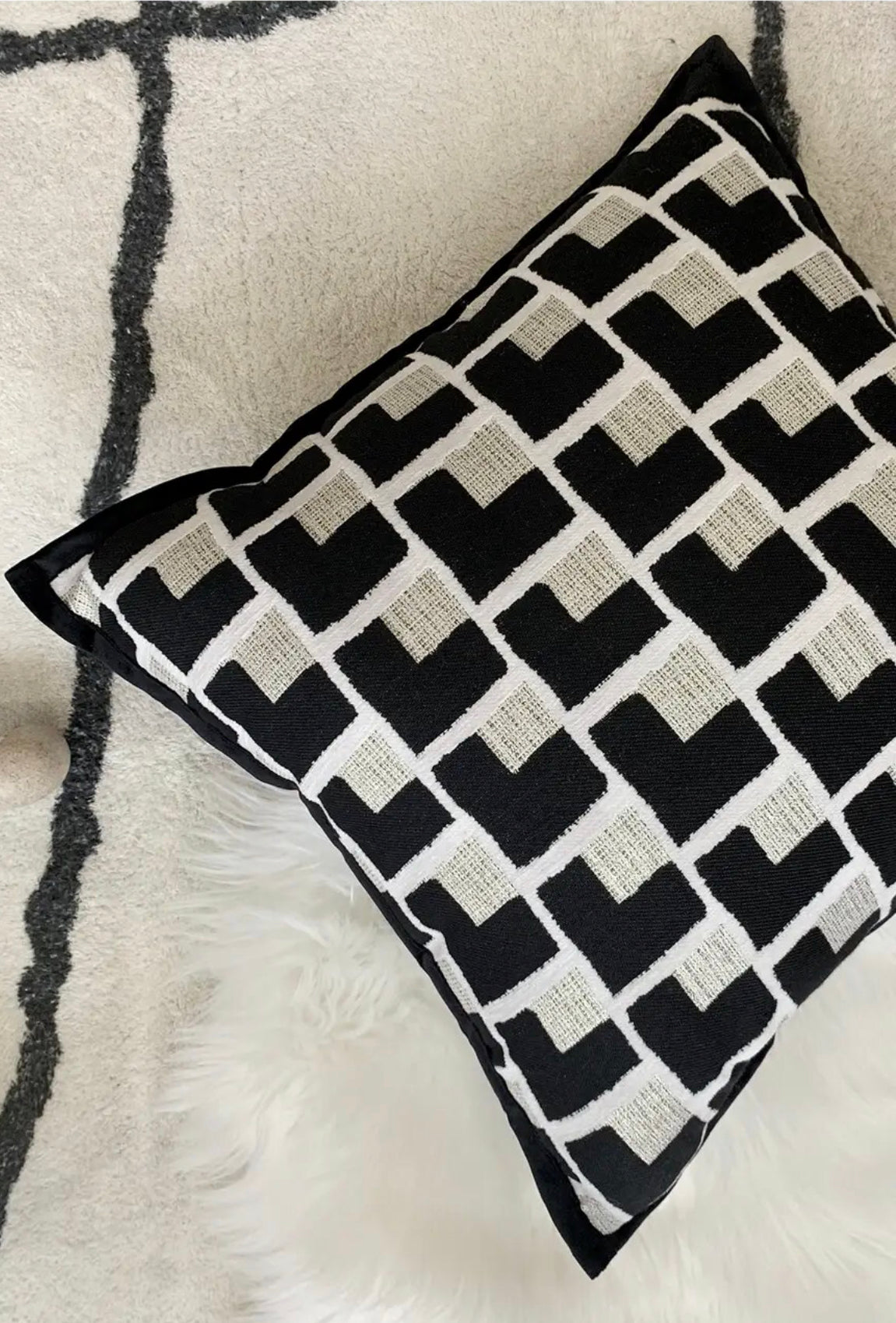 Black and cream patterned cushion styled against a pale rug