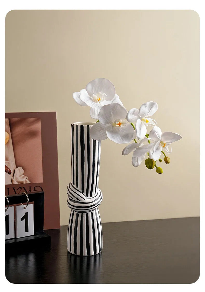 Black and white striped knot vase with white orchids next to photo frame and calendar on dark desk