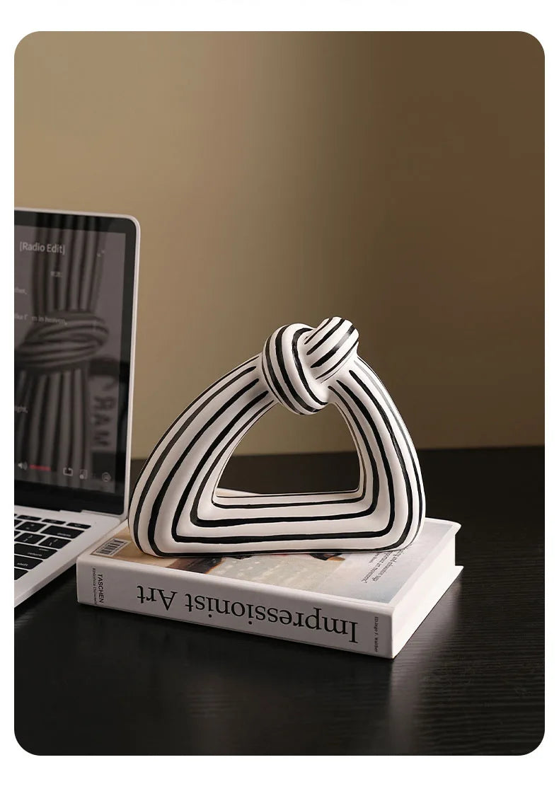 Black and white striped knot triangular ornament styled on art book next to laptop on dark desk