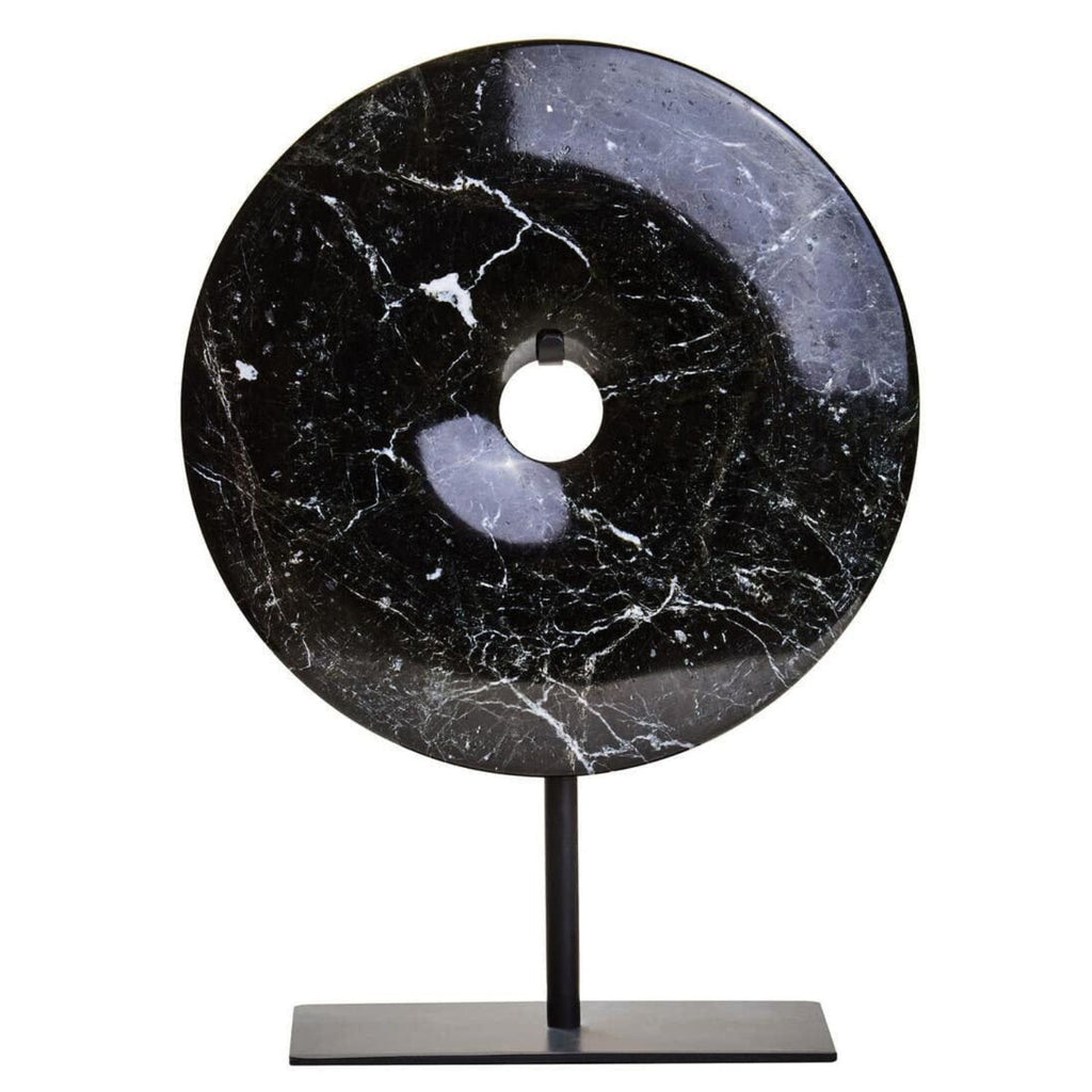 A round black stone donut sculpture with white marble veining, displayed on a minimalist black metal stand against a solid white background.