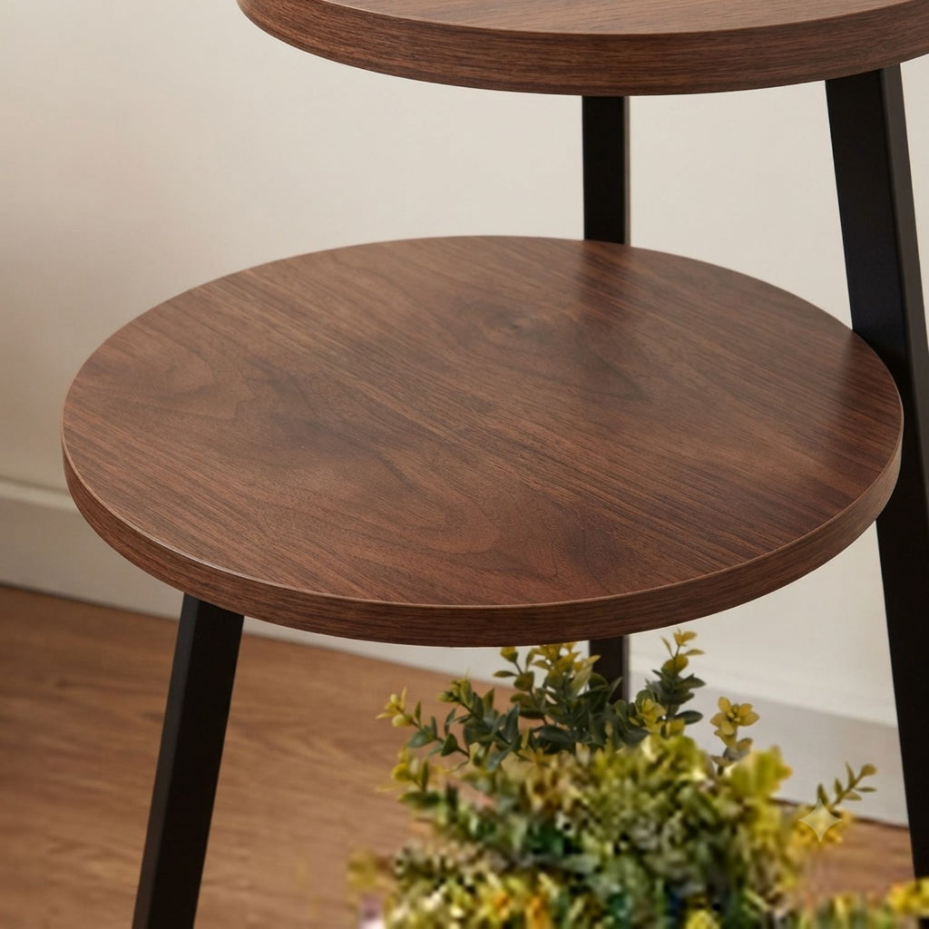 A close-up of a two-tier wooden nesting side table with dark brown wood grain circular tops and black metal legs, shown in a home interior setting.