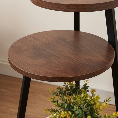 A close-up of a two-tier wooden nesting side table with dark brown wood grain circular tops and black metal legs, shown in a home interior setting.