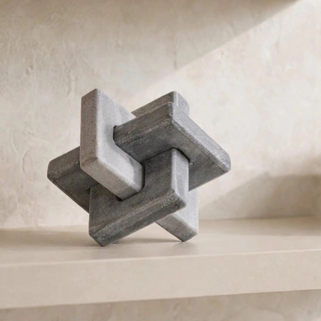 A gray stone-like geometric puzzle sculpture resting on a light beige shelf against a textured beige wall.
