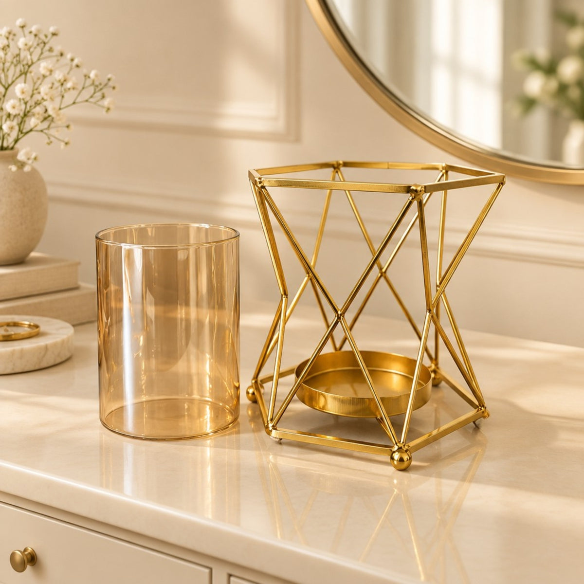 A gold geometric metal candle holder with a small gold tray inside, displayed next to a translucent amber glass candle holder on a cream-colored dresser in a beautifully styled room.