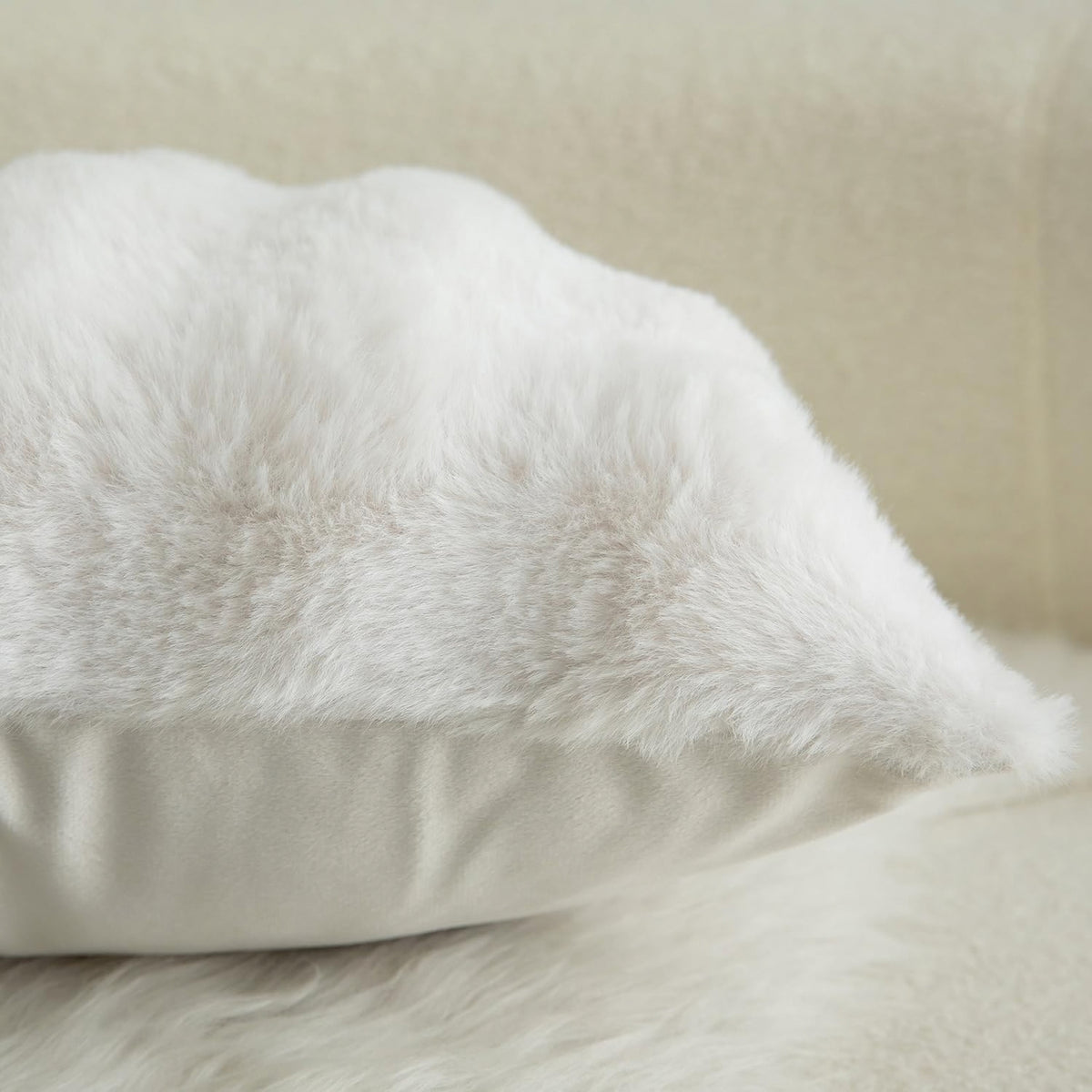 A fluffy white faux fur pillow with a smooth white fabric base, resting on a matching white faux fur surface against a soft beige background.
