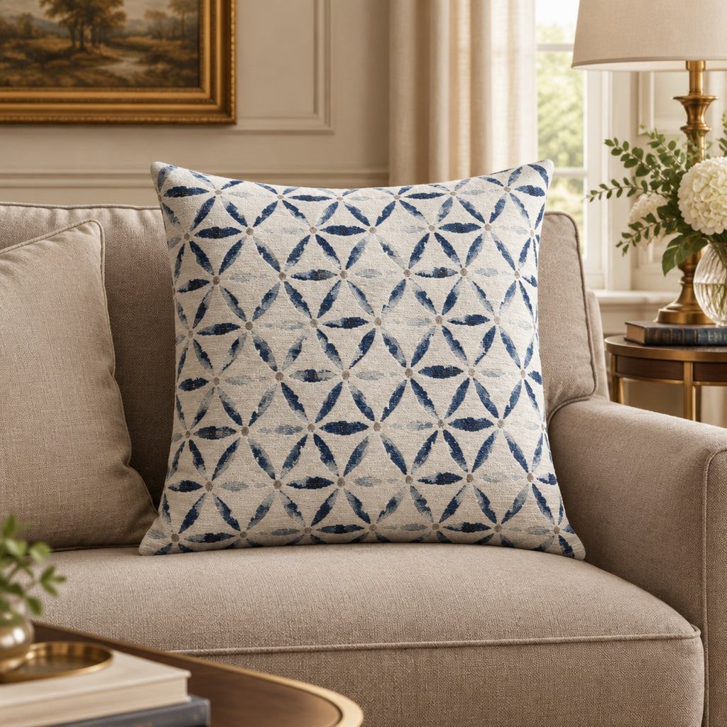 A square throw pillow with a blue and white geometric diamond pattern, styled on a beige fabric sofa in a cozy living room setting.