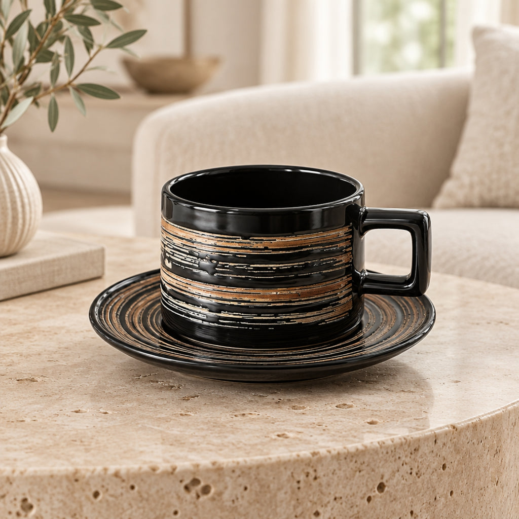 A black ceramic coffee cup with a matching saucer, featuring horizontal distressed gold and brown stripes, set on a round beige stone table in a cozy living room environment.
