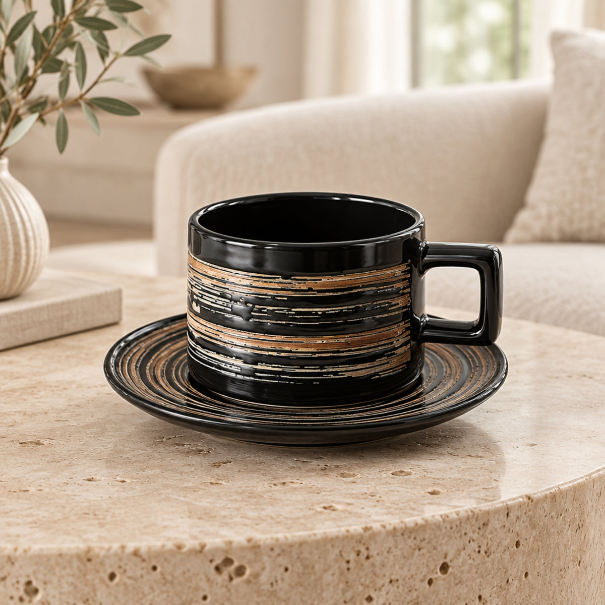 A black ceramic coffee cup with a matching saucer, featuring horizontal distressed gold and brown stripes, set on a round beige stone table in a cozy living room environment.
