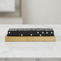 Five black dice with white pips resting on a rectangular light wood tray, placed on a white marble surface with a softly blurred neutral background.