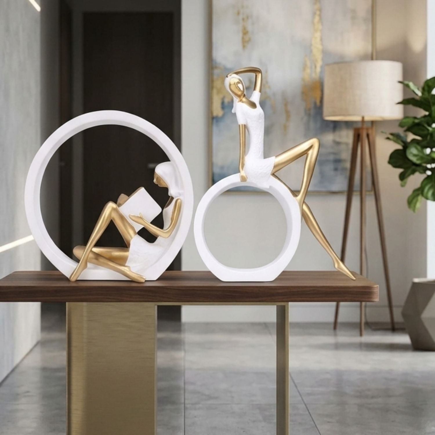 Two modern abstract figurative sculptures in white and gold, displayed on a wooden console table in a contemporary interior setting.