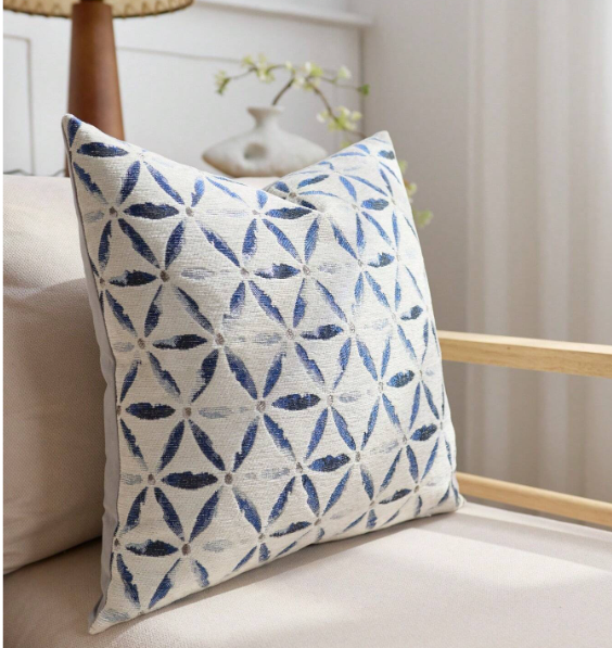 Cream square cushion with a repeating navy blue star pattern, styled on a sofa