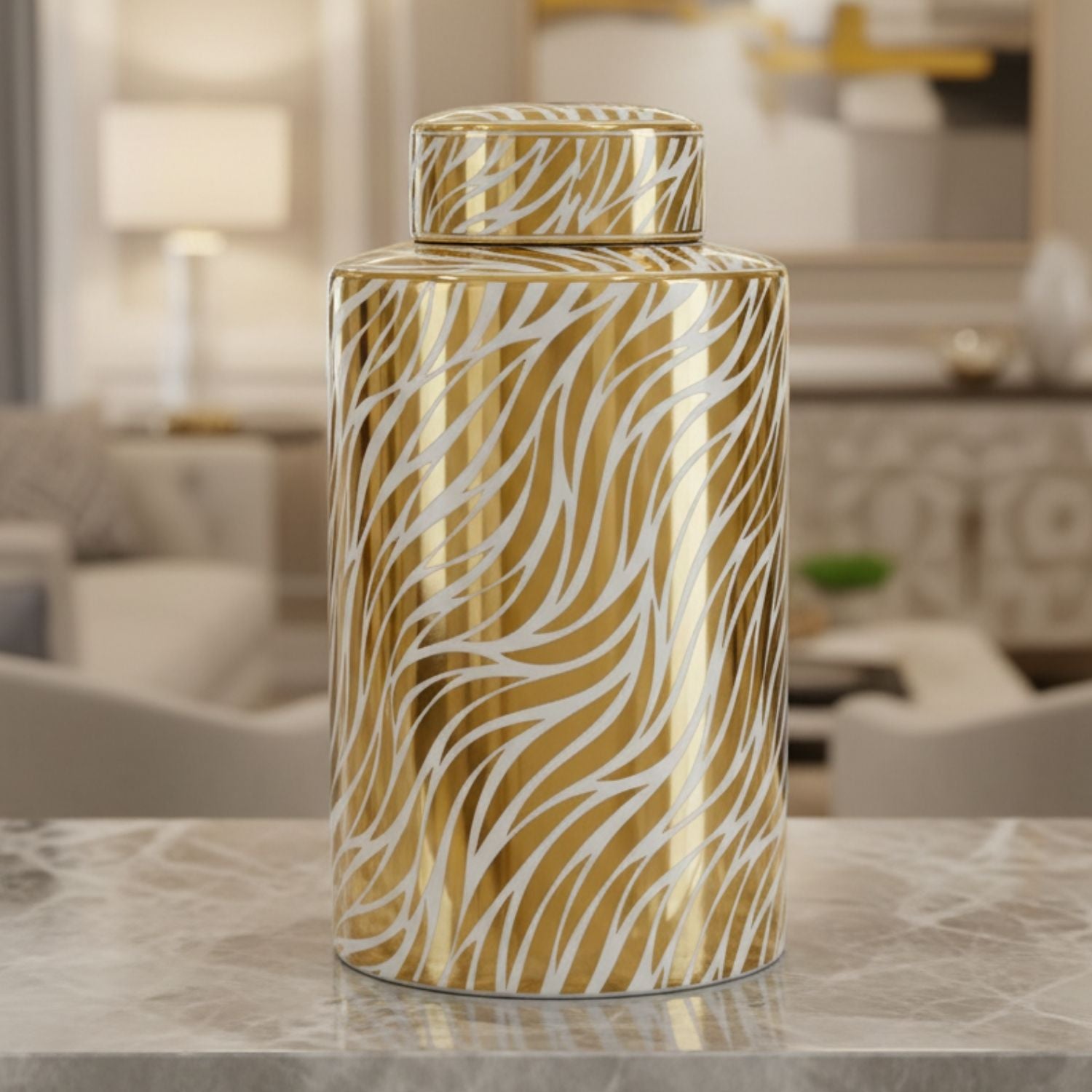 A tall cylindrical decorative canister with a matching lid, featuring a glossy gold and white zebra-stripe pattern, displayed on a marble countertop in a blurred living room setting.