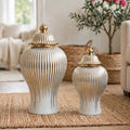 Two ribbed ceramic lidded vases in white and gold, displayed on a woven rug in a softly styled living room setting.