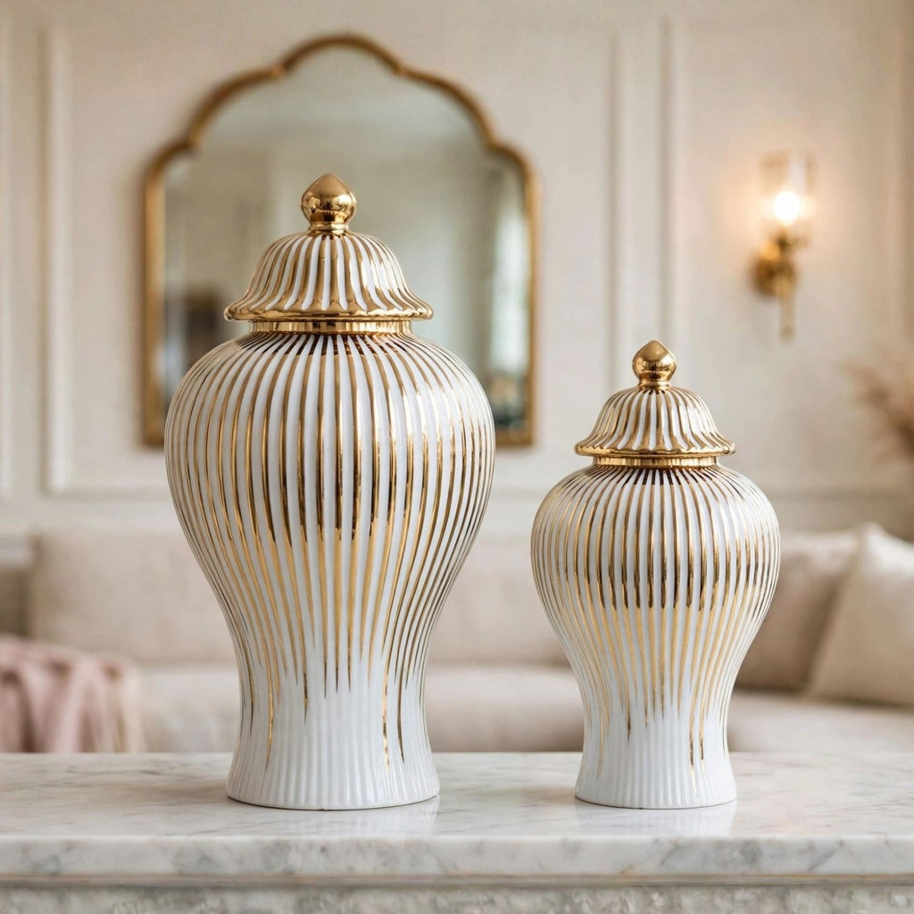 Two ribbed ceramic lidded vases in white with gold accents, displayed on a marble surface in an elegant interior setting.