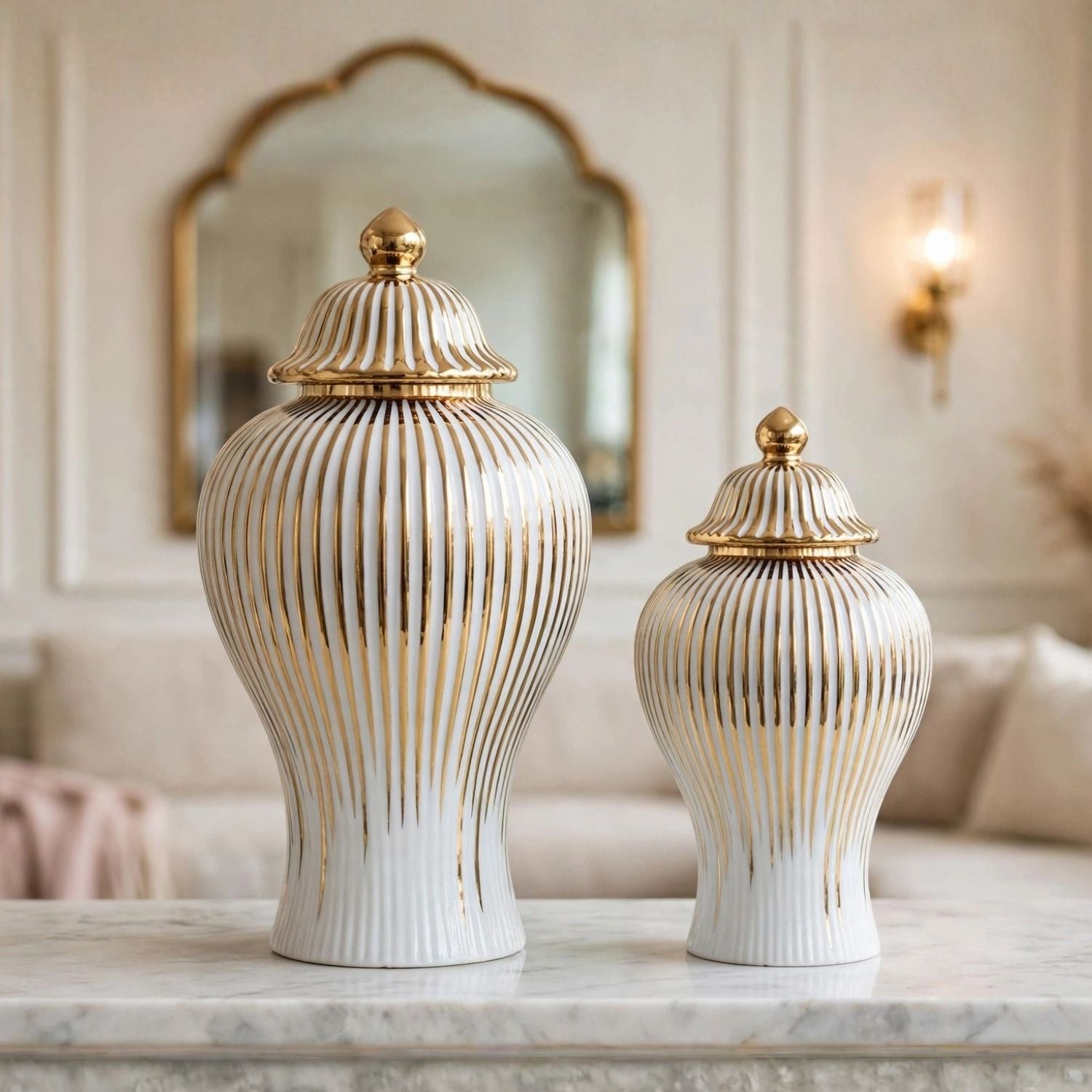 Two ribbed ceramic lidded vases in white with gold accents, displayed on a marble surface in an elegant interior setting.