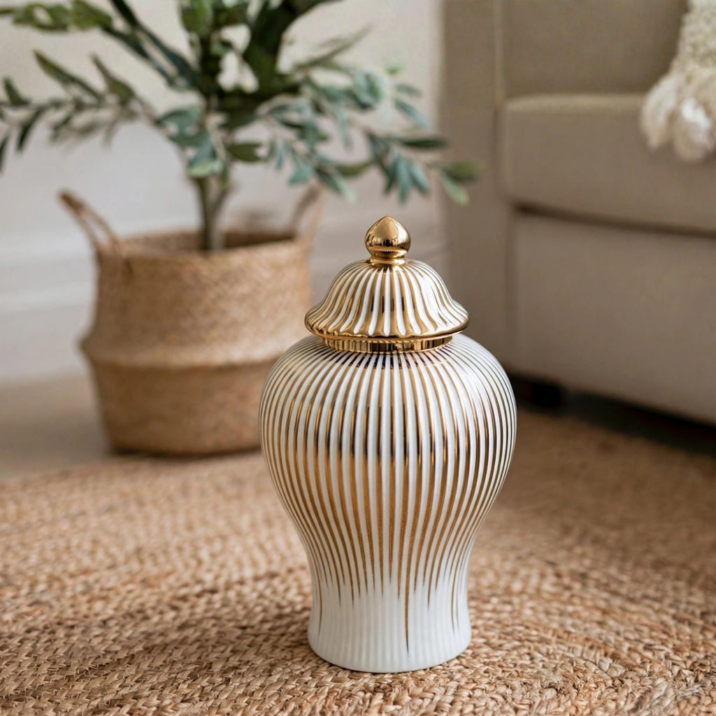 A white ceramic lidded jar with vertical gold fluted lines and a gold finial lid, placed on a woven jute rug in a living room setting.