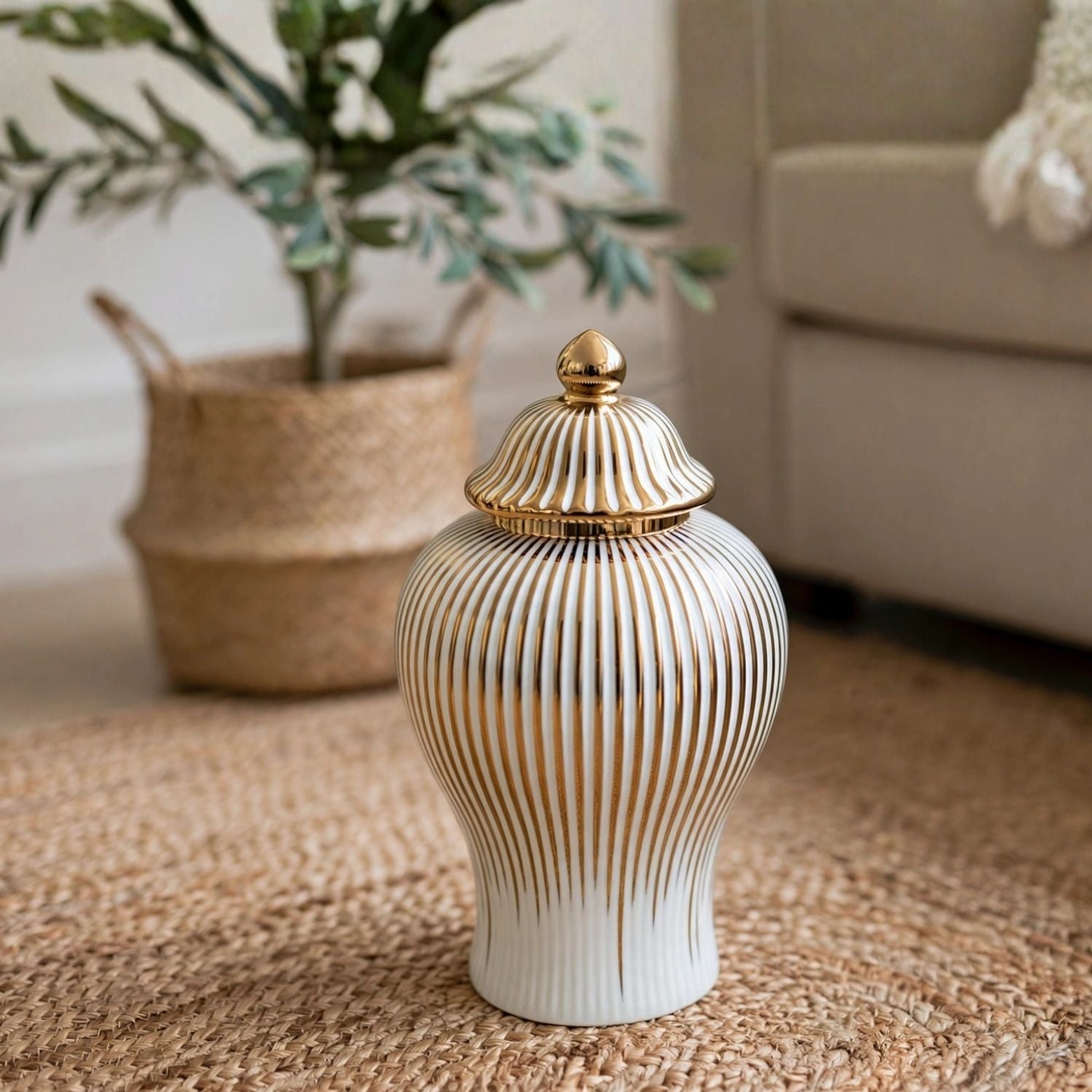 A white ceramic lidded jar with vertical gold fluted lines and a gold finial lid, placed on a woven jute rug in a living room setting.